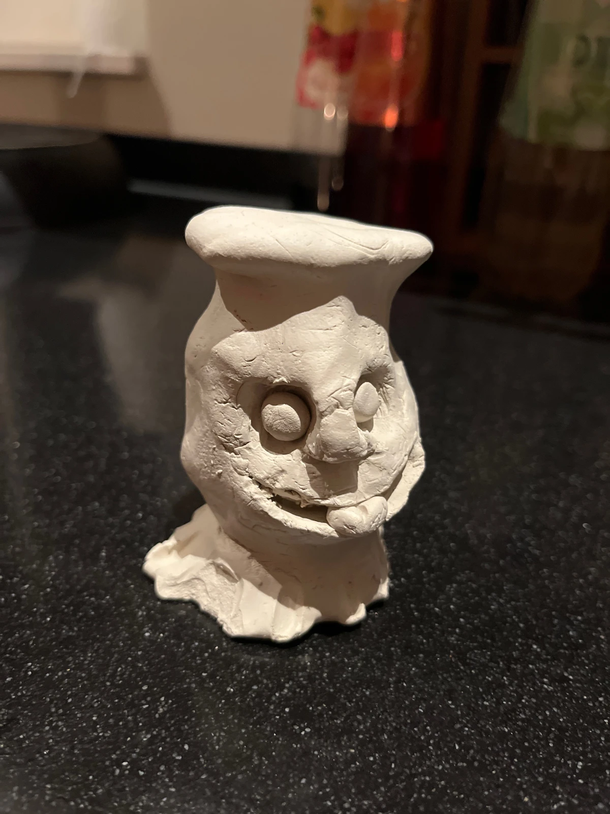 Original photo of a handmade clay face on a dark kitchen worktop
