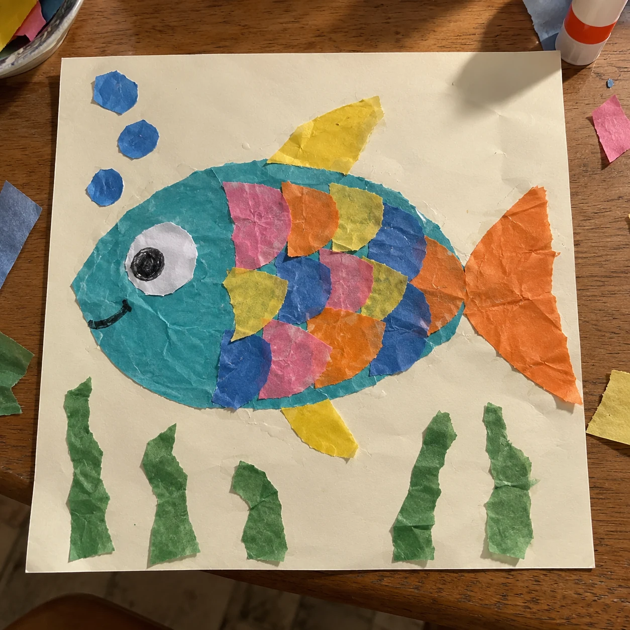 A colourful tissue-paper fish collage photographed on a craft table with shadows