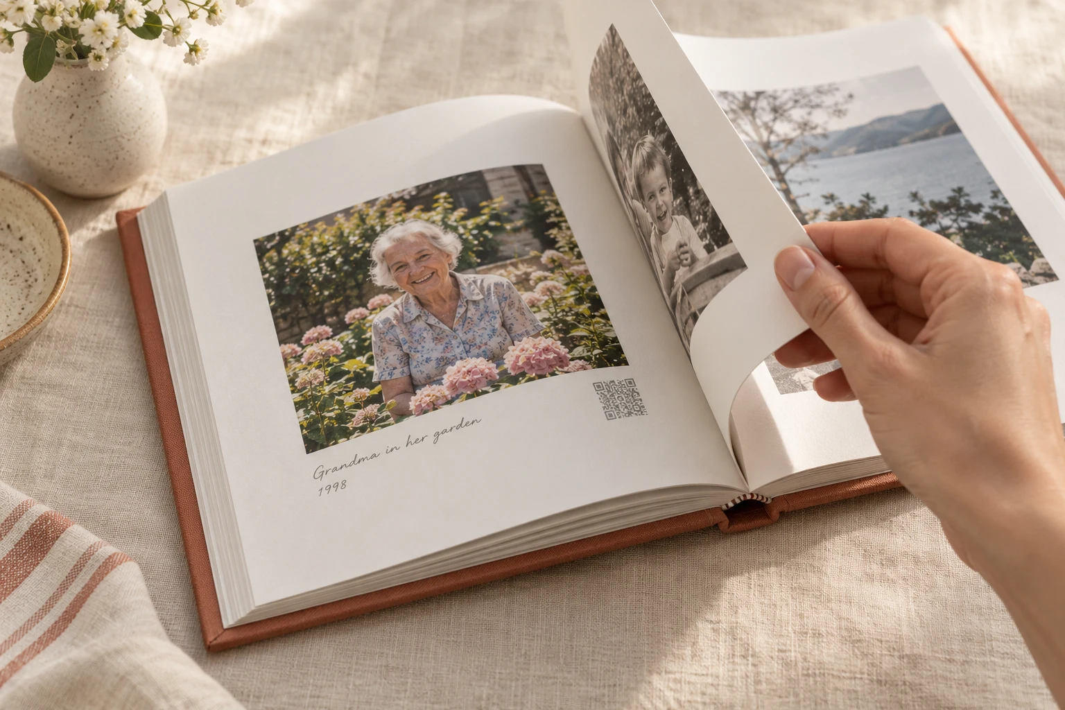 A hand turns a family memory book page with a grandmother’s garden photograph and a small printed QR code